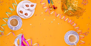 Karnaval maskesi şeklinde pudra şekerli kurabiyeler ve sarı arka planda espresso. Şölen dekoru ve tatlılar. Metin için boş alan. Yukarıdan. Pankart