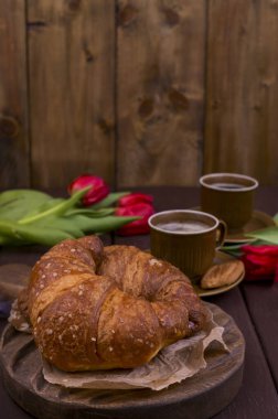 Paskalya kahvaltısında aromatik taze espresso, kruvasan, renkli yumurta, kırmızı lale ve söğüt. Kurabiyeli kahve, ahşap masadaki çiçekler. Yukarıdan bak. Boşluğu kopyala.