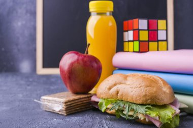 Okul öğle yemeğini okul tahtasının yanındaki bir kutuda. Salata ve peynirli sandviç, bir şişe meyve suyu, bir elma, kitaplar, bir çalar saat. Okul çocuğu için sağlıklı yemek. Metin için boş alan.