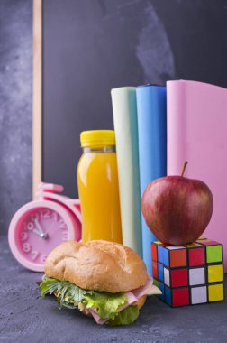 Okul öğle yemeğini okul tahtasının yanındaki bir kutuda. Salata ve peynirli sandviç, bir şişe meyve suyu, bir elma, kitaplar, bir çalar saat. Okul çocuğu için sağlıklı yemek. Metin için boş alan.