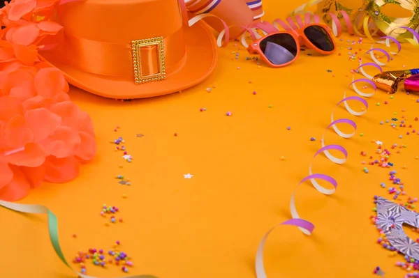 Декор для традиційного святкування Дня королів в Нідерландах. Помаранчевий капелюх, окуляри, ювелірні вироби і конфетті на яскравому тлі. Зображення у вигляді рамки. Копіюю простір. Горизонтальний формат — стокове фото