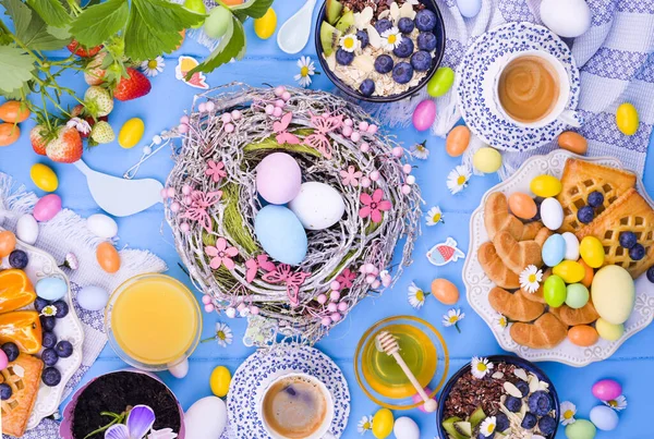 Easter breakfast flat lay. Espresso coffee, cake with jam, cookies, fresh orange juice, fruits, granola, honey, strawberries with leaves and berries on the table. Colored eggs for Easter Sunday. Stock Image