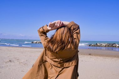 Deniz kenarındaki kız. Kahverengi saçlı kadın ufuktaki mesafeye bakıyor. Mavi gökyüzü, kumlu sahil ve dalgalı sahil. Romantik bir resim. Metin için boş alan. Boşluğu kopyala