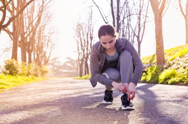 Ayakkabı bağcıklarını bağlayan koşucu kız. Güneşli bir sabahta parkta spor yapıyor. Parıltının taklidi. Çerçeve, renkli fotoğraf. Boşluğu kopyala.