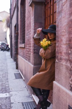 Sarı laleli şapkalı kız. Buketi olan genç bir kadın Avrupa 'nın eski şehrinde yürüyor. Turizm ve romantik yürüyüş kavramı. Yumuşak odaklanma. Uzayı kopyala Dikey fotoğraf