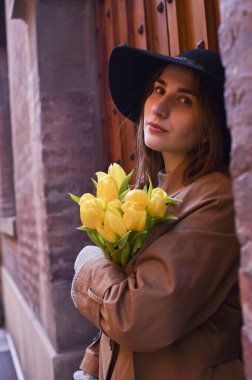 Laleli şapkalı bir kız. Buketi olan genç bir kadın Avrupa 'nın eski şehrinde yürüyor. Turizm ve romantik yürüyüş kavramı. Yumuşak odak. 