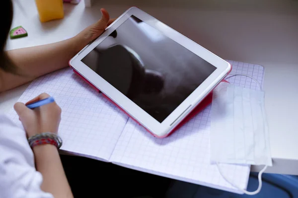 远程在线教育。在校女生在家里用笔记本电脑、数码平板电脑学习，并在笔记本上做作业。坐在房间的桌子边。软焦点 — 图库照片