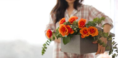 Kadın elinde gül buketi tutuyordu. Evdeki bir kutunun içinde, pencerenin kenarında. Elinde gül buketi olan bir kız. Anneler günü ve kadınlar günü kavramı. Pankart. Uzun format. Yumuşak odak