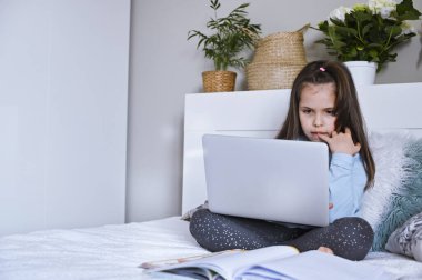 Uzaktan öğrenme çevrimiçi eğitim. Dijital tablet dizüstü bilgisayarı olan ve okul ödevi yapan kız öğrenci. Eğitim kitaplarıyla yatakta oturmak. Ev okulu. Uzayı kopyala Yatay olarak. Seçici odak