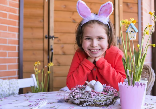 Веселая сумасшедшая девушка в кроличьи уши кролика на голове дома за столом с пасхальным украшением. Пасхальные яйца на глазах. Пасха и праздники концепция. Копирование пространства — стоковое фото