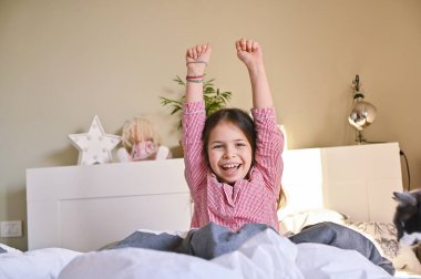 Küçük kız uyandı. Pijamalı çocuk yatakta geriniyor, gülümsüyor ve olumlu duygular gösteriyor. Sabah okula. Boşluğu kopyala