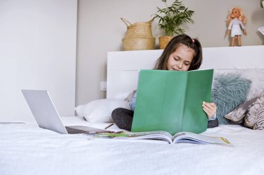 Uzaktan öğrenme çevrimiçi eğitim. Dijital tablet dizüstü bilgisayarı olan ve okul ödevi yapan kız öğrenci. Eğitim kitaplarıyla yatakta oturmak. Ev okulu. Uzayı kopyala Yumuşak odak.