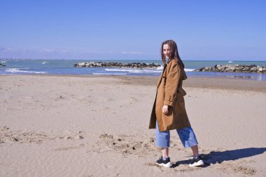 Plajın önünde duran biri. Güzel genç kız deniz kıyısında yürüyor. Duyguların dışavurumu. Turizm ve seyahat kavramı. Yüksek kalite fotoğraf