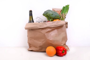 Beyaz bir arka planda yemek takımı. Karantina süresince yiyecek stokları ile dolu kağıt torba. Yiyecek teslimatı, bağış, koronavirüs. Taze sebze, meyve, zeytinyağı. Yumuşak odak.