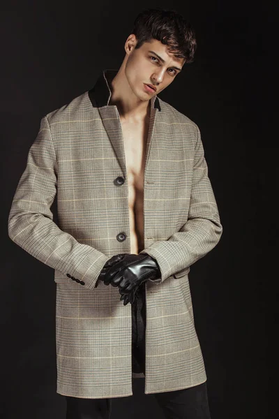 マッスル強い美しいです裸の男性モデルで黒手袋とコートでデニムジーンズで黒隔離されたフォントの背景 — ストック写真
