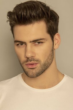 Kaslı yüz, beyaz tişörtlü güzel erkek model portresi. Gri yalıtılmış yazı tipi arka planında, gölgeli.