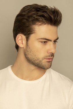 Kaslı yüz, beyaz tişörtlü güzel erkek model portresi. Gri yalıtılmış yazı tipi arka planında, gölgeli.