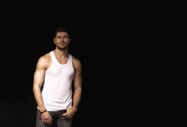 Muscle strong beautiful stripped male model with white shirt in denim gray jeans on black isolated font background
