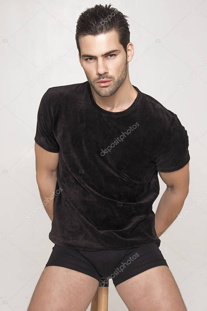Muscle strong beautiful stripped male model in black t-shirt and black underwear on grey isolated font background