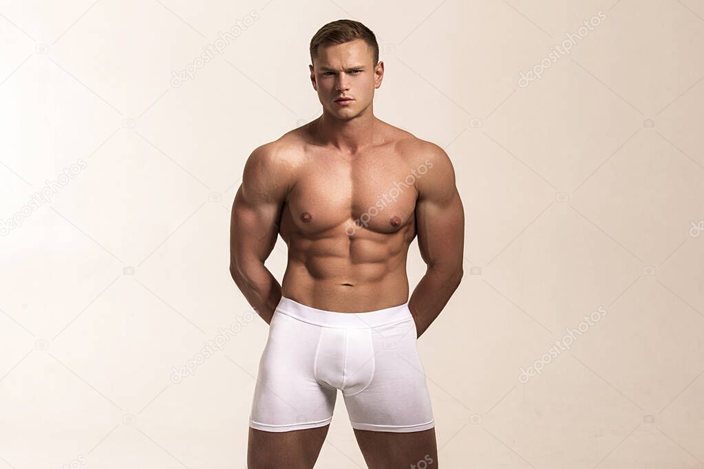 Strong stripped muscle male model in white underwear on gray isolated font background