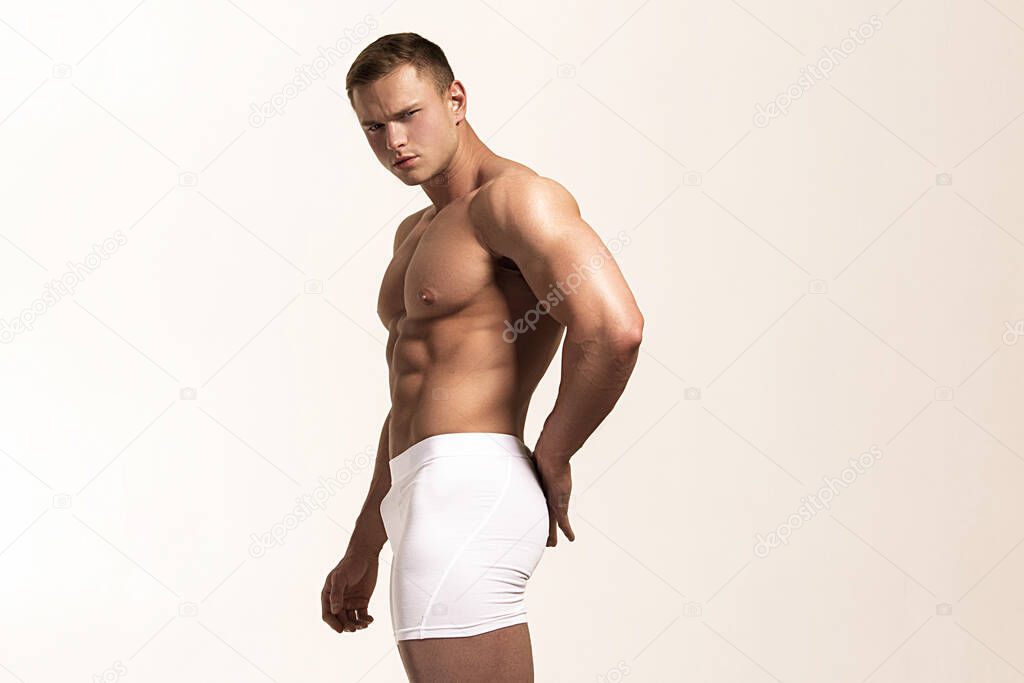 Strong stripped muscle male model in white underwear on gray isolated font background