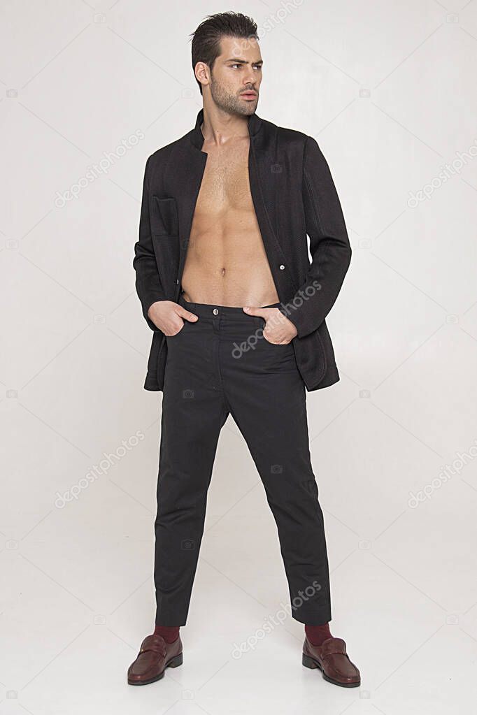 Muscle strong beautiful stripped male model in black toxedo and black trousers on grey isolated font background