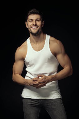 Muscle strong beautiful stripped male model with white shirt in denim gray jeans on black isolated font background