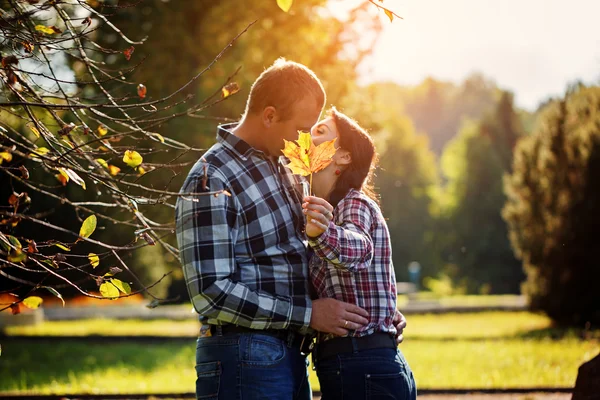 Linda pareja al aire libre en otoño. Joven hombre y mujer besándose escondidos detrás de la hoja de arce. Enfoque selectivo en —  Fotos de Stock