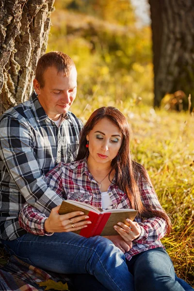 Young couple in autumn wood at picnic and reading book.