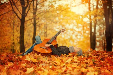 Gitar, sevimli çocuk sonbahar güneşli bir günde çim üzerinde yalan