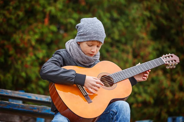 Kleiner Junge spielt Gitarre an einem herbstlichen kalten Tag. er ist bekleidet mit einem — Stockfoto