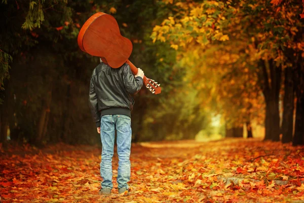 Chlopak z gitara spaceru na szlaku jesienią. Widok z tyłu — Zdjęcie stockowe