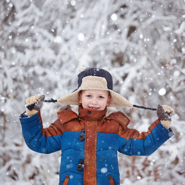 Menino bonito, criança em roupas de inverno andando sob a neve no parque de inverno . — Fotografia de Stock