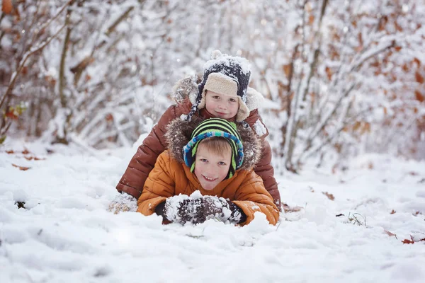 Dwa małe dzieci, chłopak braci gry i leżącego śniegu na zewnątrz podczas opadów śniegu. Aktywny wypoczynek z dziećmi w zimie — Zdjęcie stockowe