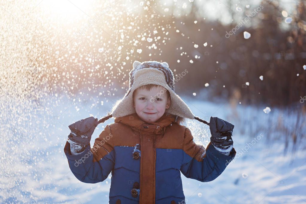 Winter little child playing throws up snow outdoors during snowfall. Active outoors leisure with children in winter on cold snowy days