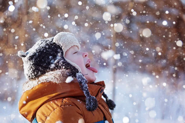 Retrato de un lindo niño con ropa de abrigo que atrapa la boca de copos de nieve en invierno día soleado . — Foto de Stock