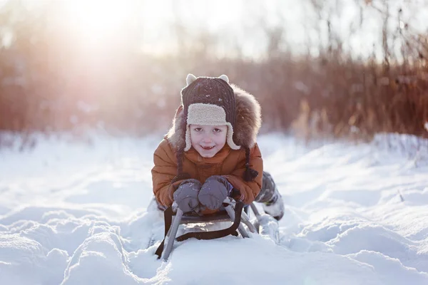 Lindo niño divertido en ropa de invierno caliente divertirse en trineo de nieve, al aire libre durante la nevada . — Foto de Stock