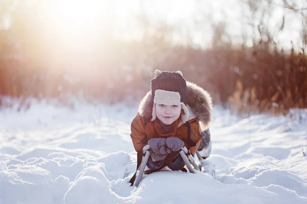 Roztomilý malý legrační dítě chlapec v teplé zimní oblečení baví na sáňky, venku během sněžení. Stock Snímky