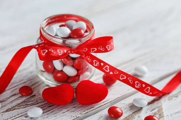 カラフルなキャンディの瓶木製白地赤弓心飾られています。バレンタインの日の概念 — ストック写真