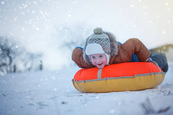 Lindo chico deslizándose con tubería en la nieve, invierno, concepto de felicidad . — Foto de Stock