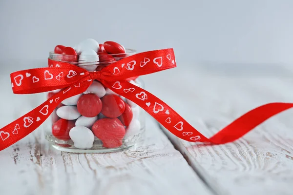 Yürekleri Beyaz ahşap zemin üzerinde kırmızı bir yay ile dekore edilmiş renkli şeker kavanoz. — Stok fotoğraf