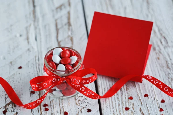 軽い木製の背景に赤いリボンで飾られたカラフルなキャンディの瓶とバレンタイン カード. — ストック写真