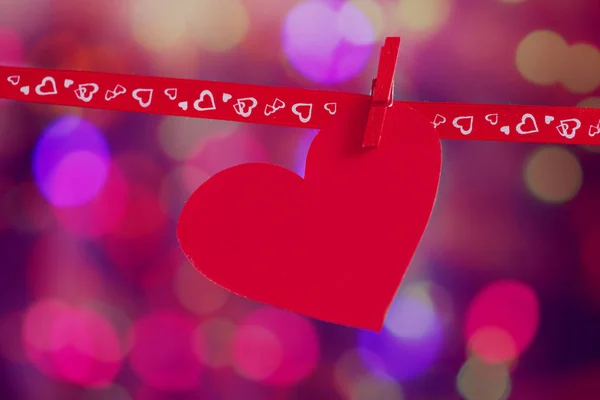 Κόκκινο χαρτί καρδιά κρέμονται στην κόκκινη κορδέλα στο πολύχρωμο φόντο. Ημέρα του Αγίου Βαλεντίνου έννοια, Toned εικόνας — Φωτογραφία Αρχείου