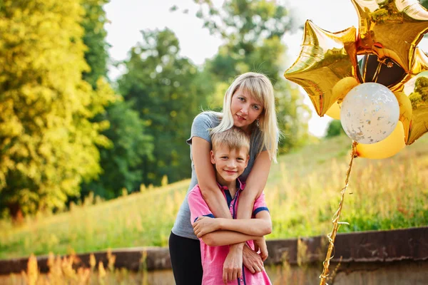 Mother and her little son with gold balloons in summer day. Happy family mom and kid hugging — Stock Photo, Image