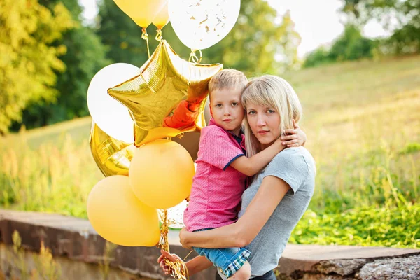 母と夏の日の金の風船と彼女の幼い息子。幸せ家族ママと子供を抱いて — ストック写真