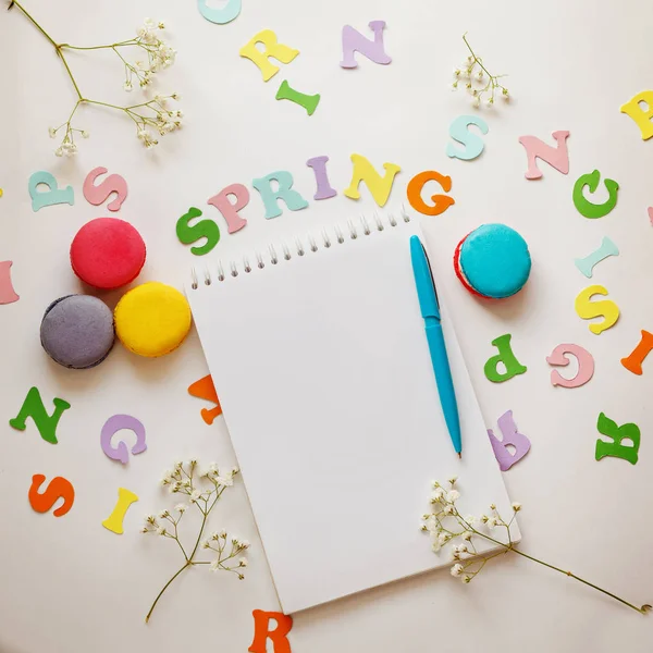 Vista dall'alto immagine della parola primaverile, notebook vuoto aperto e macaron colorati . — Foto Stock