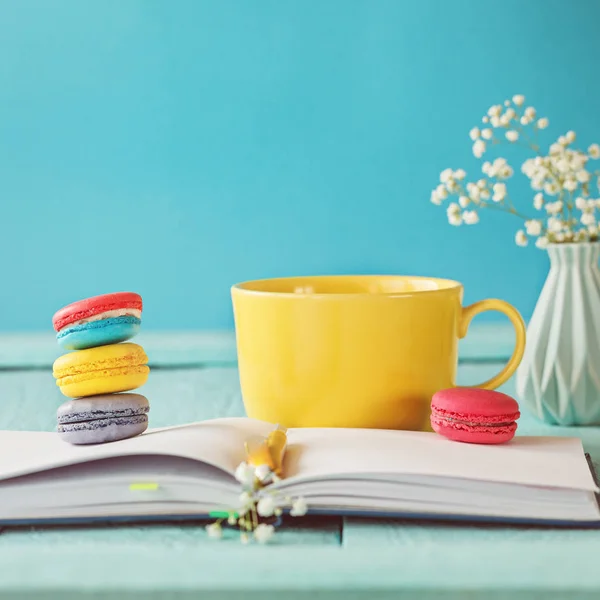 Grote gele kopje thee met bloem en bitterkoekjes en laptop op blauwe achtergrond — Stockfoto