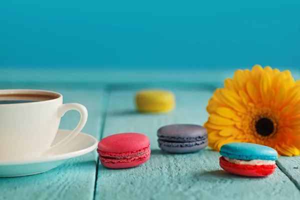 Чашка кофе или чая с желтым цветком и макаронами на синем фоне — стоковое фото