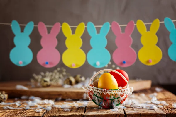 Пасхальная композиция пасхальных красочных яиц в корзине и с гирляндой кролика на деревянном фоне . — стоковое фото