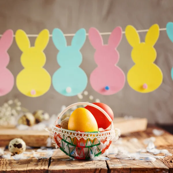 Composizione pasquale di uova colorate pasquali nel cesto e con ghirlanda di coniglio su sfondo di legno . — Foto Stock